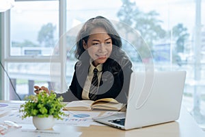 Smiling mature middle aged business woman using laptop working and sitting at desk