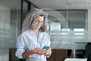 Smiling mature professional business woman entrepreneur using phone in office.