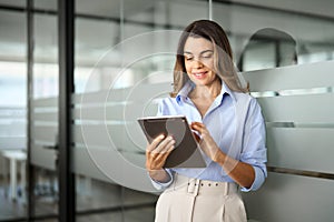 Smiling mature professional business woman using tablet standing in office.