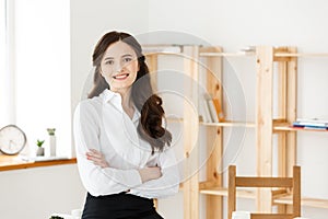 Smiling mature professional businesswoman with arms crossed sitting on the desk in office.