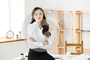 Smiling mature professional businesswoman with arms crossed sitting on the desk in office.