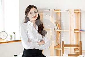 Smiling mature professional businesswoman with arms crossed sitting on the desk in office.