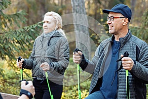 Smiling mature, senior people group learning Scandinavian, Nordic walking with professional sticks in forest, chatting