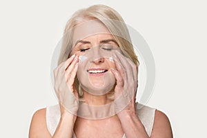 Smiling mature woman applying rejuvenating cream on her face skin