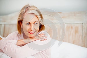 Smiling mature woman in bed and looking away - copyspace. Closeup portrait of a smiling mature woman in bed and looking