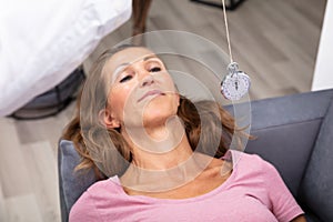 Woman Being Hypnotized With Pendulum Lying On Sofa photo