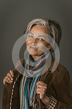 Smiling mature woman in casual. Female portrait on gray. Lady wearing colorfull scarf and jacket smiles looking at