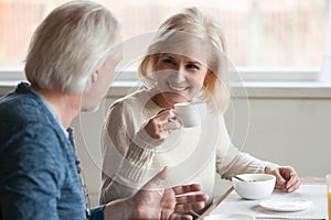 Smiling mature woman drinking coffee listening to elderly man ta