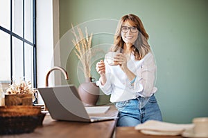 Smiling mature woman drinking her coffee in the kitchen at home