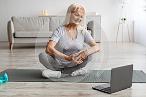 Smiling mature woman exercising on yoga mat using laptop