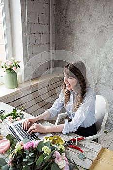 Smiling Mature Woman Florist Small Business Flower Shop Owner. She is using her telephone and laptop to take orders for