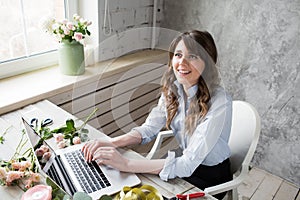 Smiling Mature Woman Florist Small Business Flower Shop Owner. She is using her telephone and laptop to take orders for