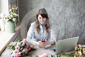 Smiling Mature Woman Florist Small Business Flower Shop Owner. She is using her telephone and laptop to take orders for
