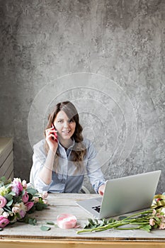 Smiling Mature Woman Florist Small Business Flower Shop Owner. She is using her telephone and laptop to take orders for