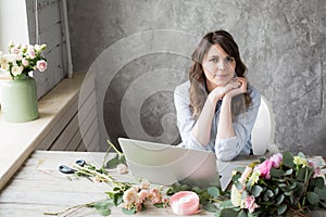 Smiling Mature Woman Florist Small Business Flower Shop Owner. She is using her telephone and laptop to take orders for