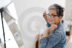 Smiling mature woman in glasses looks in the mirror, natural beauty