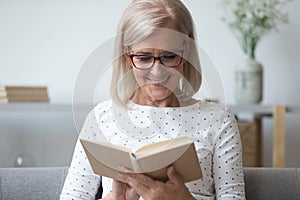 Smiling mature woman in glasses reading book close up