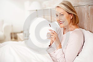 Smiling mature woman having tea or coffee in bed. Portrait of a smiling mature woman having tea or coffee in bed.