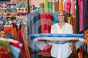 Smiling mature woman holding cloth rolls in her fabric shop