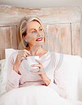 Smiling mature woman holding coffee mug in bed. Portrait of a smiling mature woman holding coffee mug in bed.