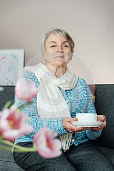 Smiling mature woman holding cup of tea, relaxing at home, positive senior female sitting on couch in modern living room