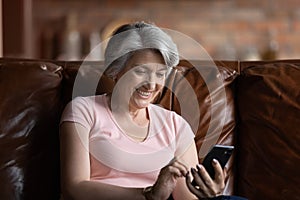 Smiling mature woman holding smartphone, surfing internet at home