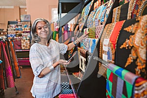 Smiling mature woman looking at colorful fabric in her shop