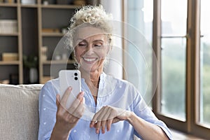 Smiling mature woman in modern wireless earphones using smartphone