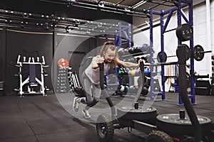 Smiling mature woman pushing a sled during a gym workout