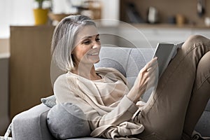 Smiling mature woman read book relaxing on couch at home