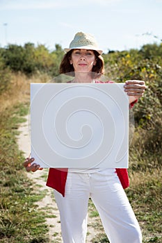 Smiling mature woman showing blank sign for teasing in countryside photo