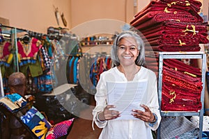 Smiling mature woman standing in her fabric shop reading paperwork