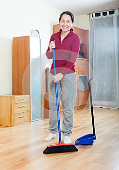 Smiling mature woman sweeping the floor