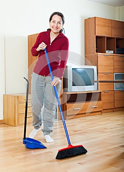 Smiling mature woman sweeping the floor