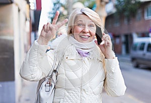 Smiling mature woman talking on phone and hand up