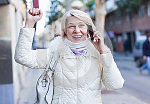 Smiling mature woman talking on phone and hand up