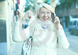Smiling mature woman talking on phone and hand up