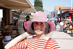 Smiling mature woman try straw hat in street market shop