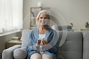 Smiling mature woman use mobile phone sitting on couch