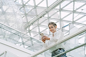 Smiling mature woman using mobile phone while standing in modern art gallery