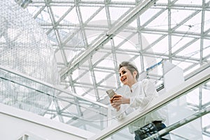 Smiling mature woman using mobile phone while standing in modern art gallery