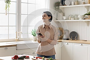 Smiling mature woman using modern smartphone in the kitchen