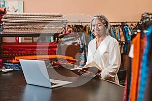 Smiling mature woman at work in her colorful fabric store