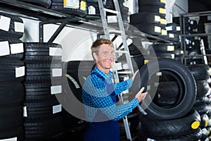 Smiling mechanic man standing with car tires