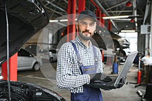 Smiling mechanic using a laptop pc at the repair garage.