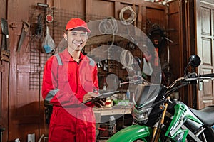 Smiling mechanic wearing wearpack and hat using digital tablet standing near the dirt bike