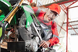 Smiling mechanic wearing wearpack and hat using a wrench to tighten the motorcycle bolt