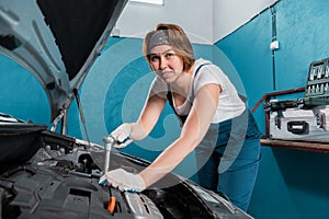 Smiling mechanic woman in blue coveralls repair a engine with ratchet wrench. The concept of woman& x27;s equality and