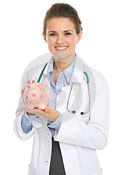 Smiling medical doctor woman holding piggy bank