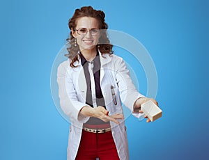 Smiling medical practitioner woman showing soap bar on blue